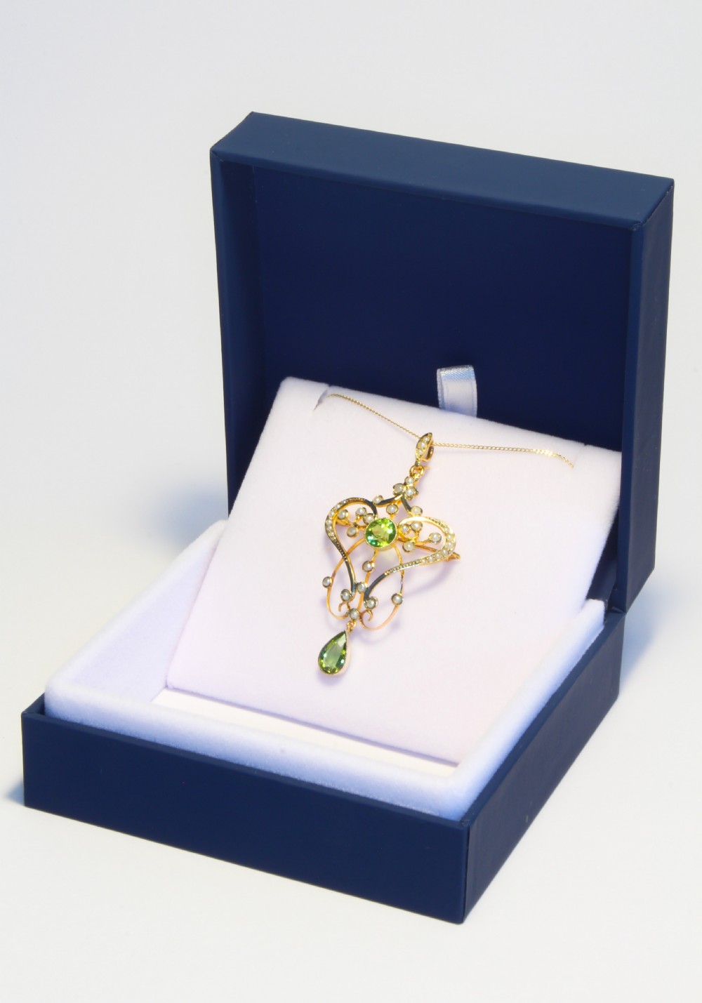 An openwork gold Art Nouveau pendant featuring curved scrollwork set with seed pearls, a central circular green peridot, and a hanging pear-cut peridot drop. View V
