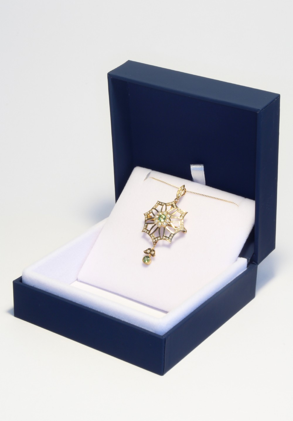 An openwork gold starburst pendant brooch set with seed pearls and a central round peridot, featuring a suspended drop peridot. View II