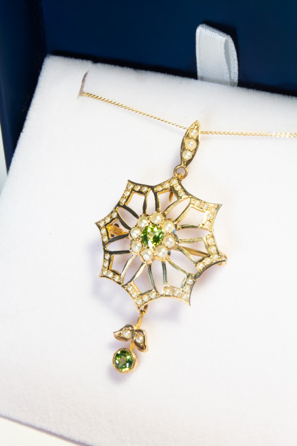 An openwork gold starburst pendant brooch set with seed pearls and a central round peridot, featuring a suspended drop peridot. View III