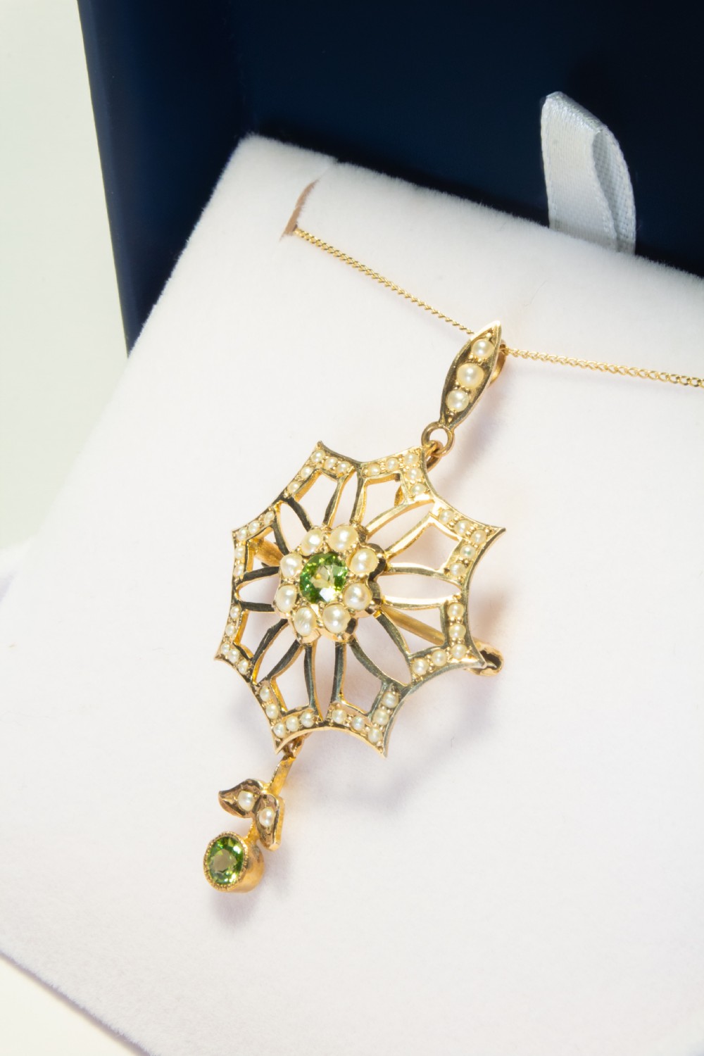 An openwork gold starburst pendant brooch set with seed pearls and a central round peridot, featuring a suspended drop peridot. View IV