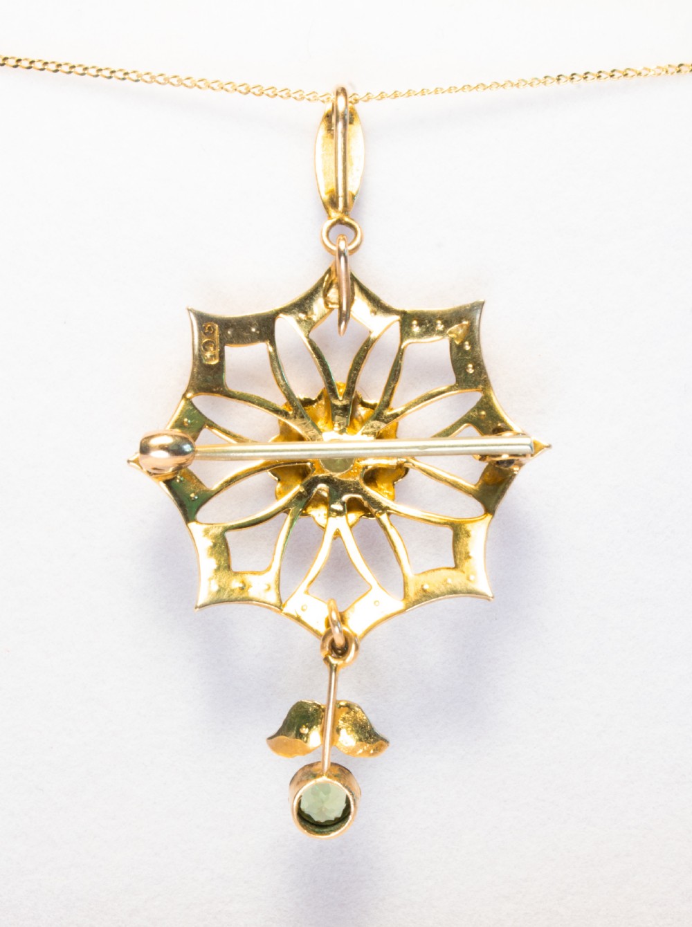 An openwork gold starburst pendant brooch set with seed pearls and a central round peridot, featuring a suspended drop peridot. View V