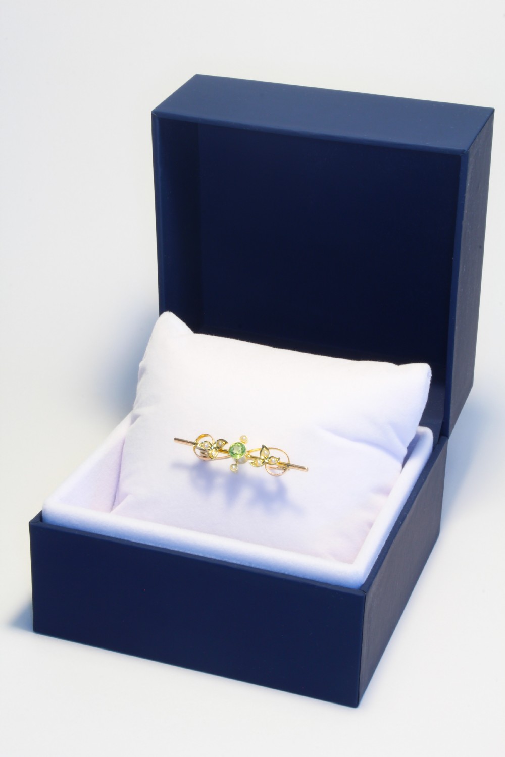 An early 20th-century 9ct gold bar brooch featuring a central round facetted green peridot flanked by foliate leaf motifs set with seed pearls. View II
