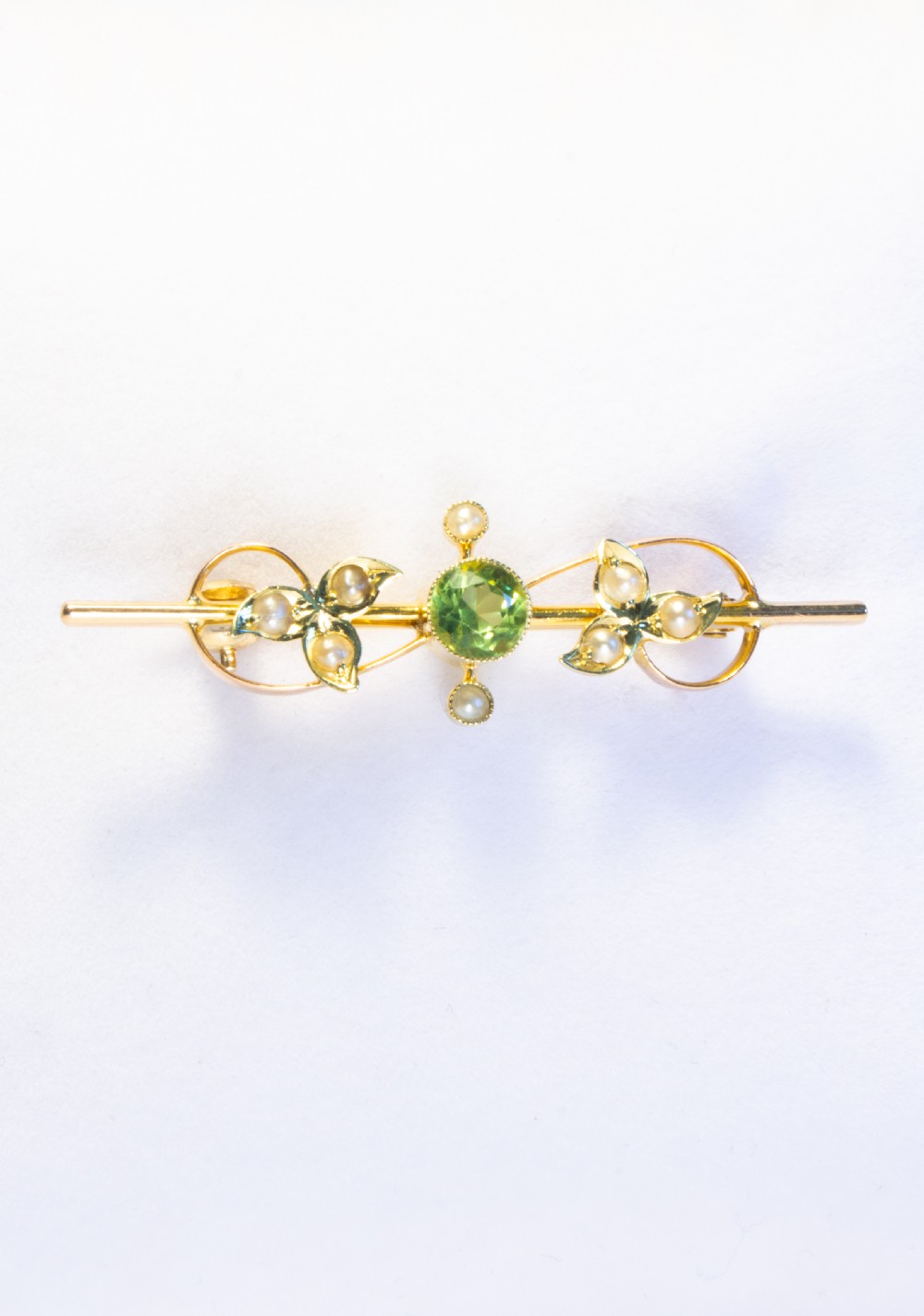An early 20th-century 9ct gold bar brooch featuring a central round facetted green peridot flanked by foliate leaf motifs set with seed pearls. View III