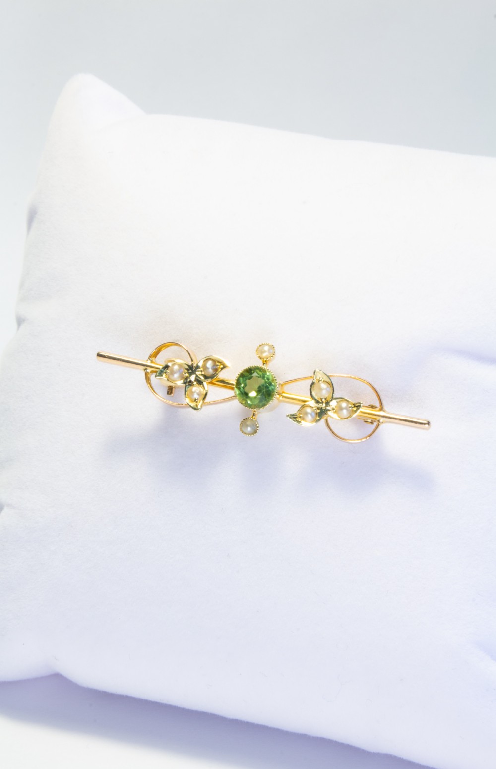 An early 20th-century 9ct gold bar brooch featuring a central round facetted green peridot flanked by foliate leaf motifs set with seed pearls. View IV