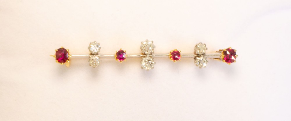 An early 20th-century bar brooch in gold set with an alternating linear row of red rubies and white diamonds in claw settings.