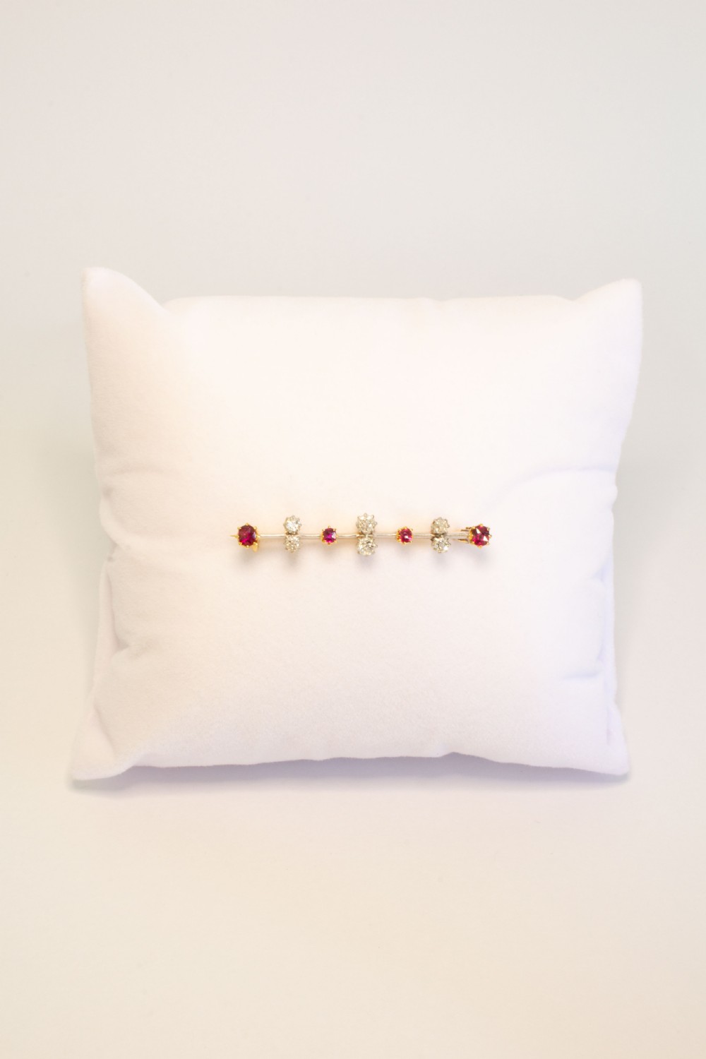 An early 20th-century bar brooch in gold set with an alternating linear row of red rubies and white diamonds in claw settings. View II