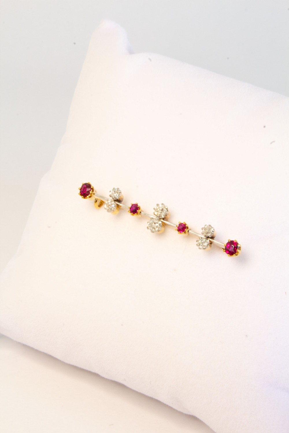 An early 20th-century bar brooch in gold set with an alternating linear row of red rubies and white diamonds in claw settings. View IV