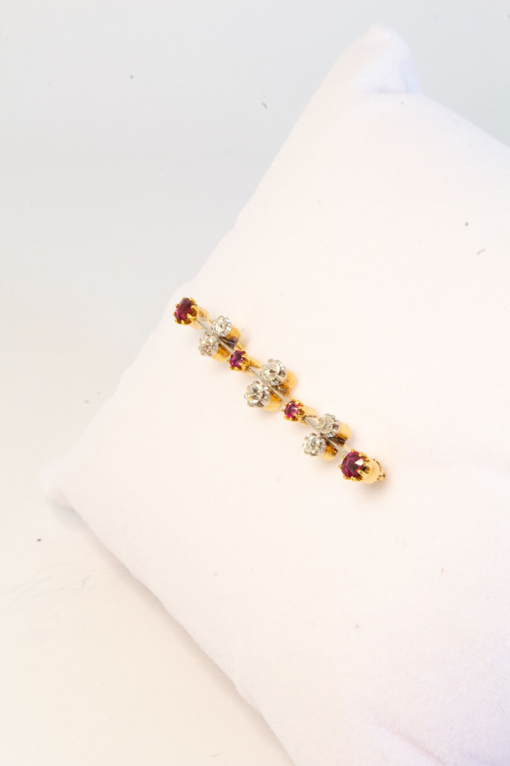 An early 20th-century bar brooch in gold set with an alternating linear row of red rubies and white diamonds in claw settings. View V
