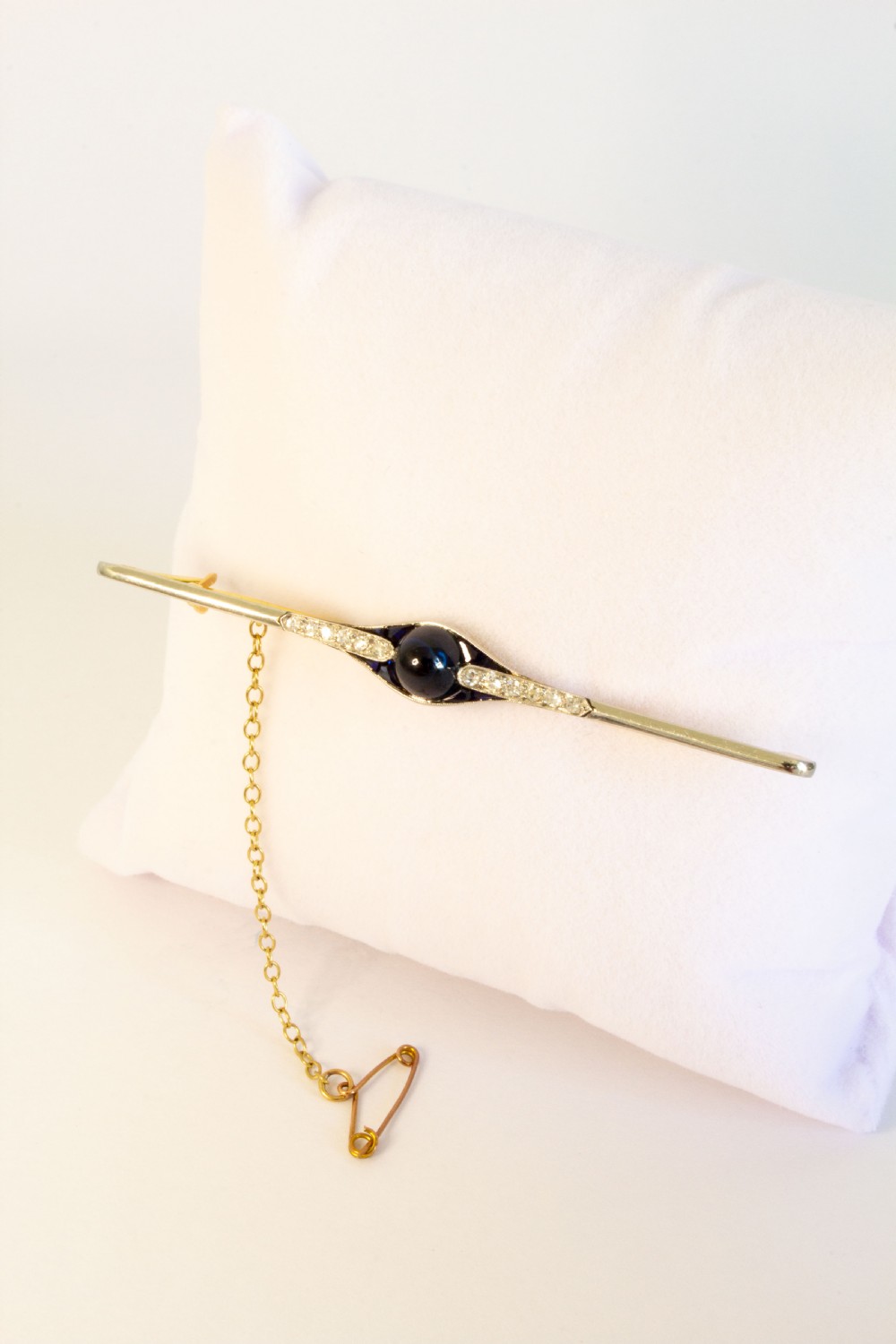 An 18ct gold and platinum bar brooch featuring a central dark cabochon sapphire flanked by small diamonds and calibre-cut sapphires with an attached safety chain. View III