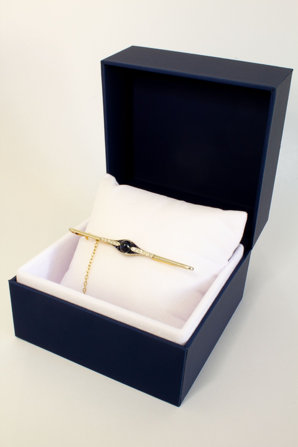 An 18ct gold and platinum bar brooch featuring a central dark cabochon sapphire flanked by small diamonds and calibre-cut sapphires with an attached safety chain. View V