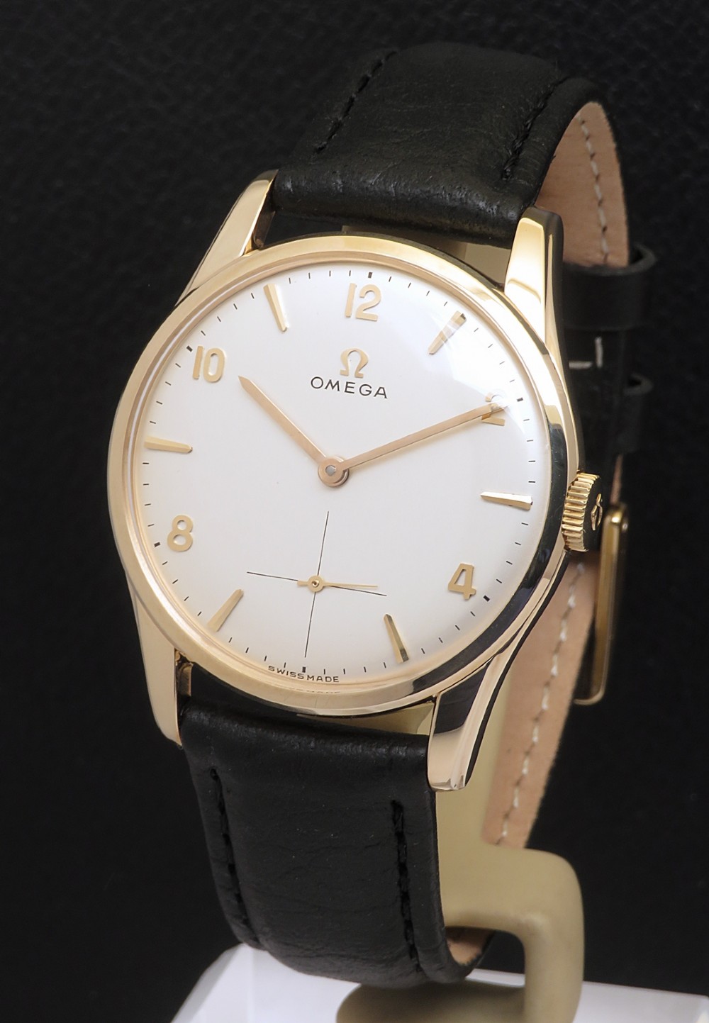 A 1964 Omega wristwatch featuring a solid 9ct yellow gold circular case, white dial with gold hour markers and sub-seconds dial, and a black leather strap.