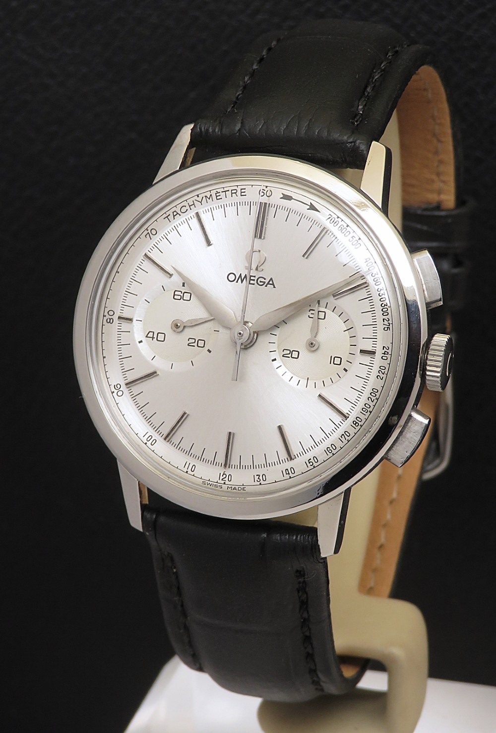 A 1963 stainless steel Omega chronograph wristwatch featuring a silver dial with two sub-dials and a black leather strap.