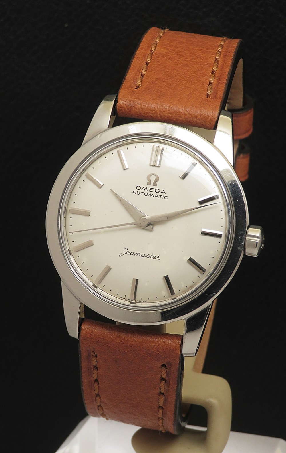 A 1950 vintage Omega Seamaster automatic wristwatch featuring a stainless steel case, cream dial with silver index markers, and a stitched tan leather strap.