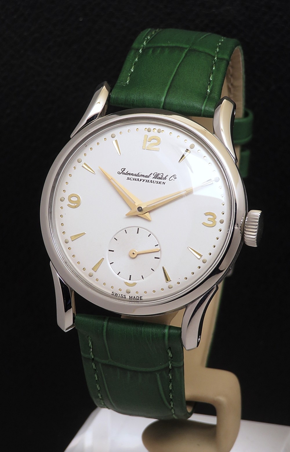 A vintage Swiss wristwatch featuring a stainless steel case, white dial with gold-tone markers, sub-seconds subdial, and a green leather strap.