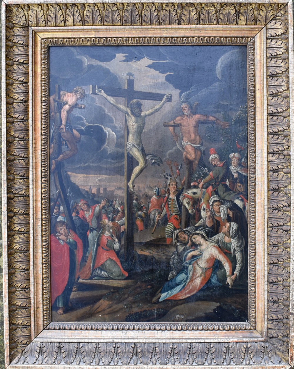 An 18th-century Netherlandish oil painting depicting the Crucifixion of Christ set within an ornate carved giltwood frame.
