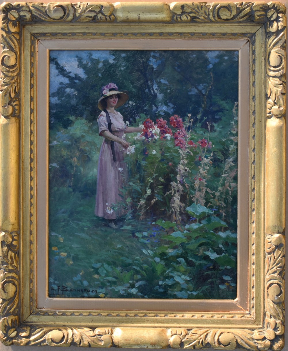 An oil painting depicting a woman wearing a straw hat and pink dress standing in a lush green garden, framed in an ornate gold giltwood frame.