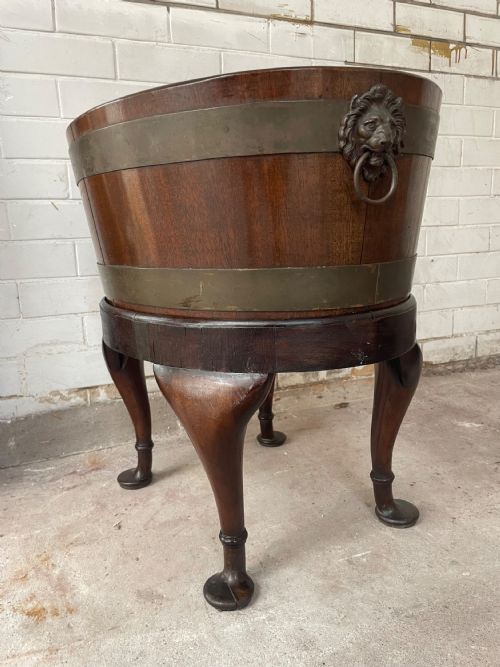 fig 1. An oval brass-bound mahogany wine cooler on a stand with cabriole legs, pad feet, and lion mask handles.