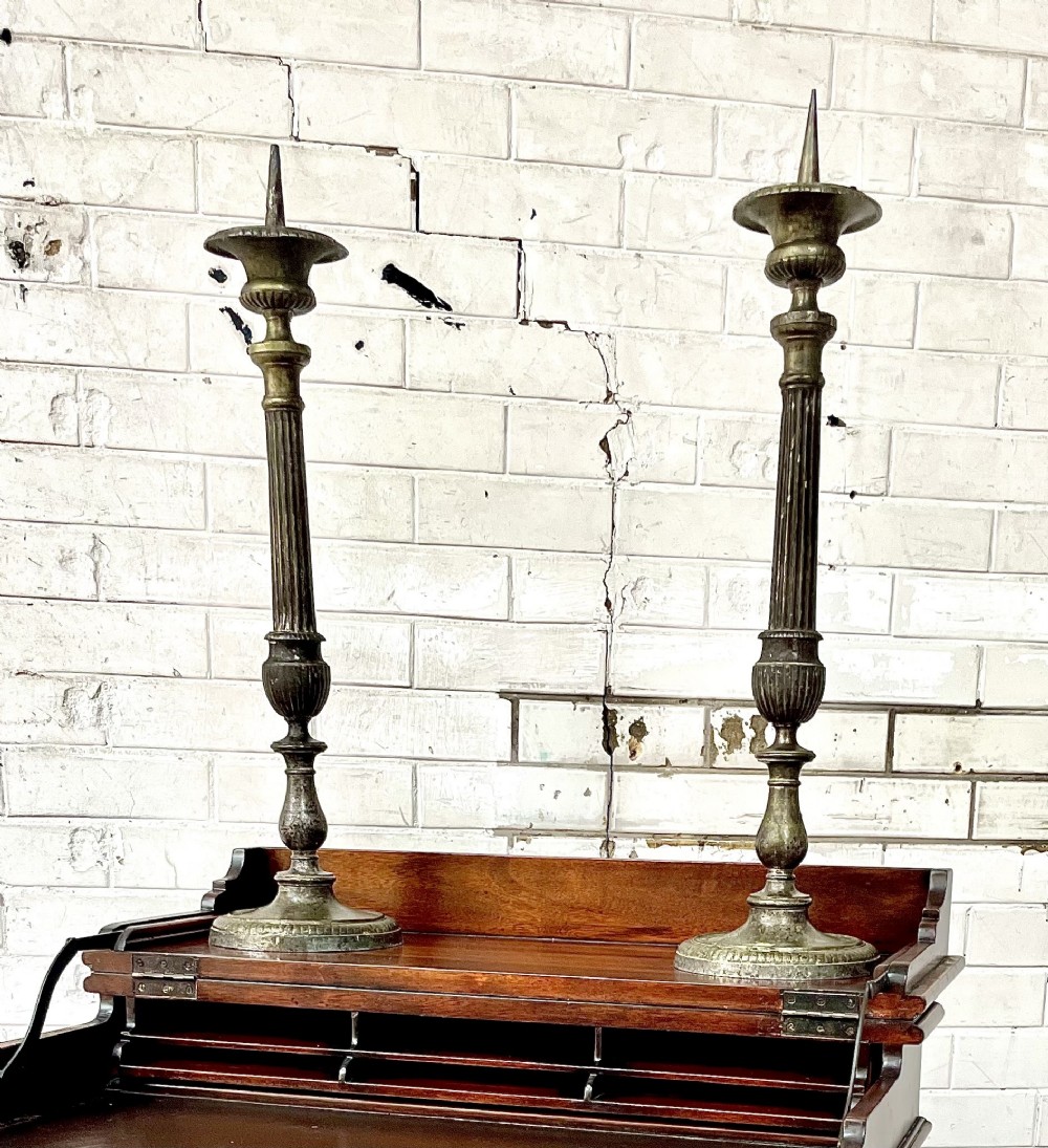 A pair of tall aged brass pricket candlesticks featuring fluted central columns, flared drip trays, top candle spikes, and circular patterned bases.