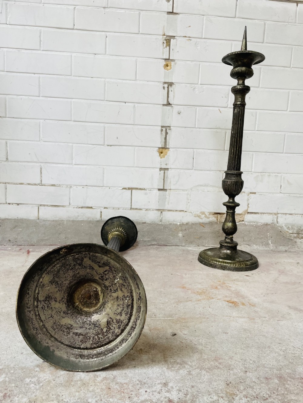 A pair of tall aged brass pricket candlesticks featuring fluted central columns, flared drip trays, top candle spikes, and circular patterned bases. View IV
