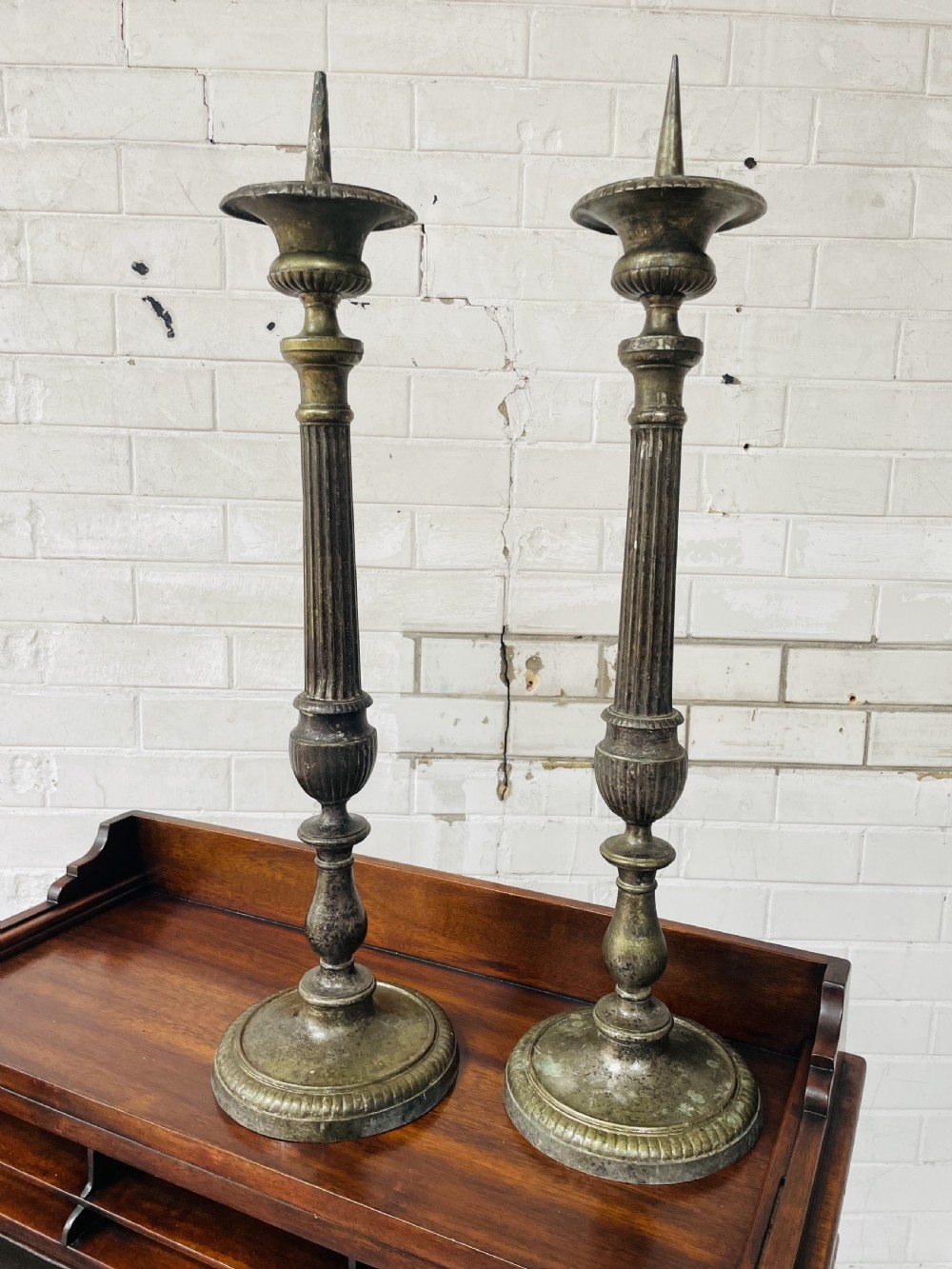 A pair of tall aged brass pricket candlesticks featuring fluted central columns, flared drip trays, top candle spikes, and circular patterned bases. View VIII
