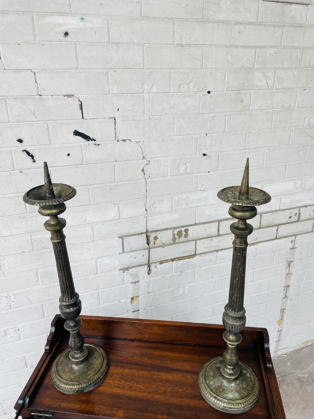 A pair of tall aged brass pricket candlesticks featuring fluted central columns, flared drip trays, top candle spikes, and circular patterned bases. View IX