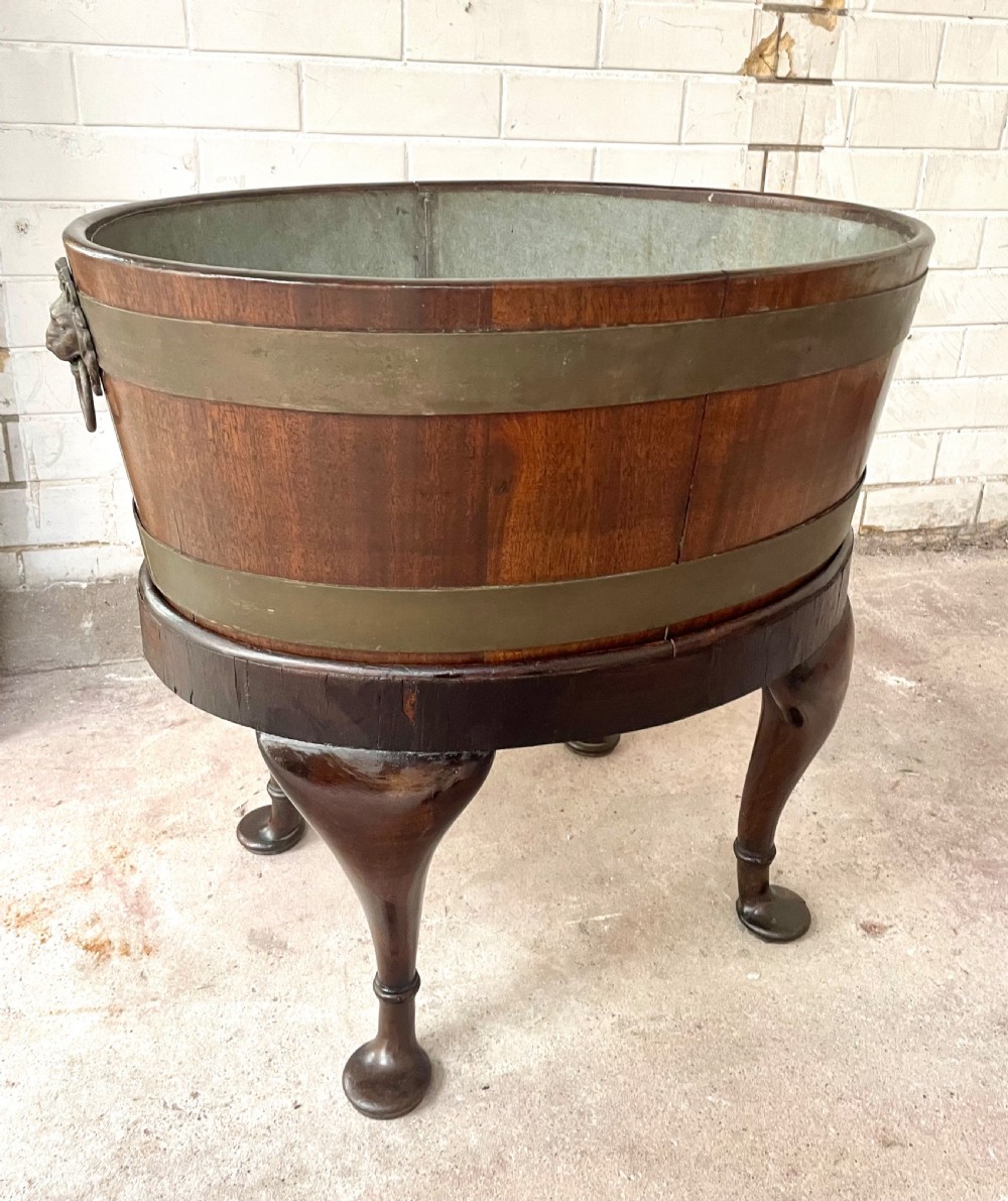 An oval brass-bound mahogany wine cooler on a stand with cabriole legs, pad feet, and lion mask handles. View V