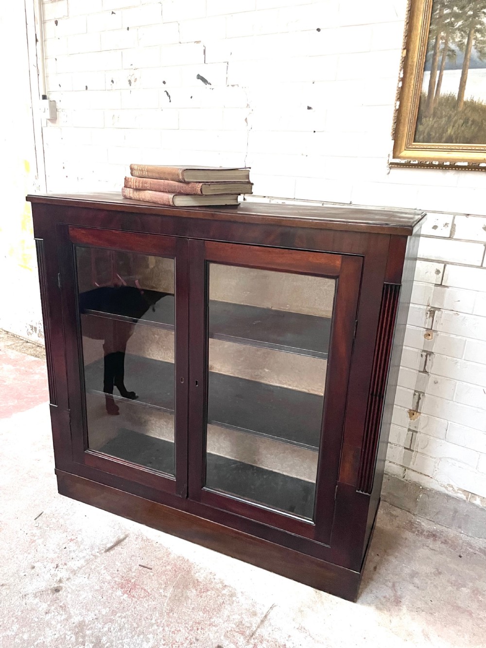 A low dark mahogany glazed bookcase featuring two glass panel doors, fluted side pilasters, and an integrated plinth base. View III