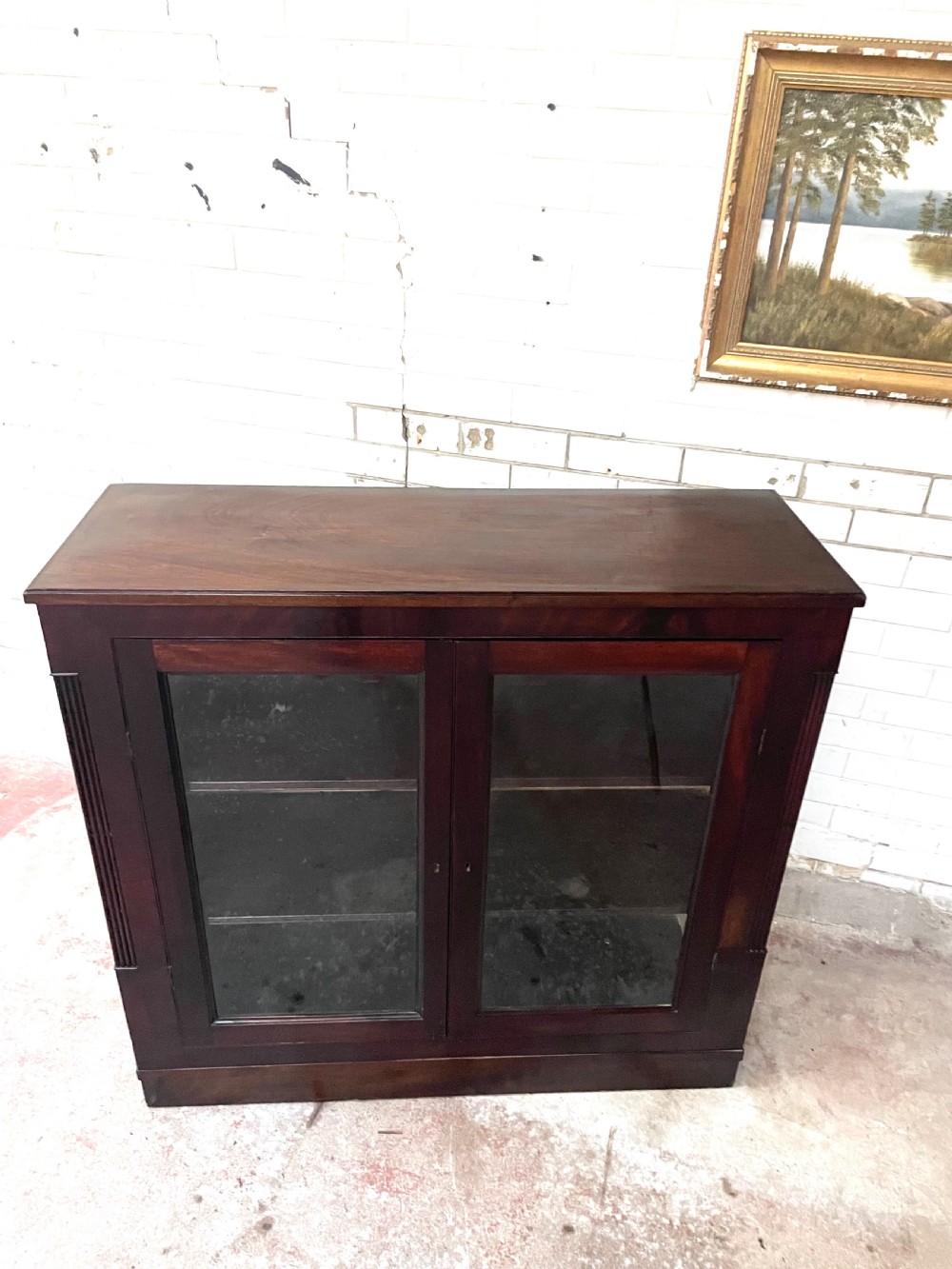 A low dark mahogany glazed bookcase featuring two glass panel doors, fluted side pilasters, and an integrated plinth base. View VII