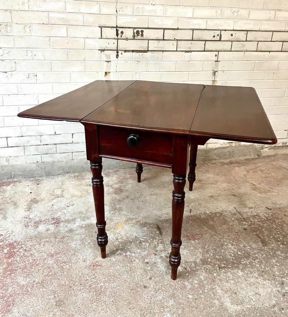 A Victorian mahogany drop-leaf table with extended side flaps, a central drawer with a turned black knob, and four turned legs.