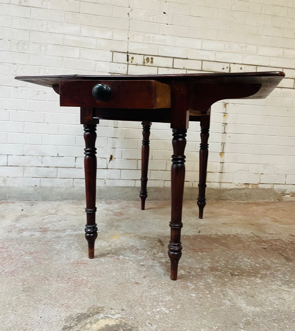 A Victorian mahogany drop-leaf table with extended side flaps, a central drawer with a turned black knob, and four turned legs. View VII