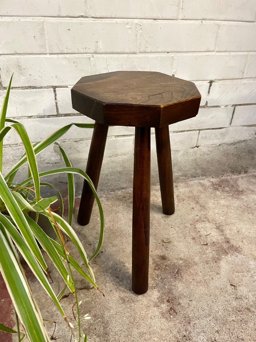 A dark oak three-legged milking stool featuring a thick octagonal seat top and splayed tapered legs.