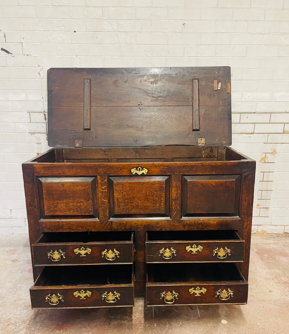 An 18th-century dark oak mule chest featuring three raised front panels above four brass-handled drawers, supported by stile feet. View II