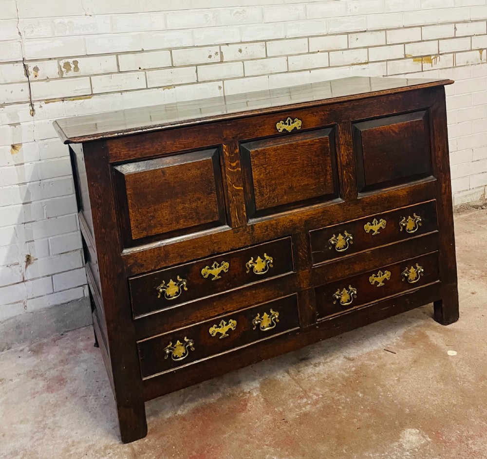 An 18th-century dark oak mule chest featuring three raised front panels above four brass-handled drawers, supported by stile feet. View IV