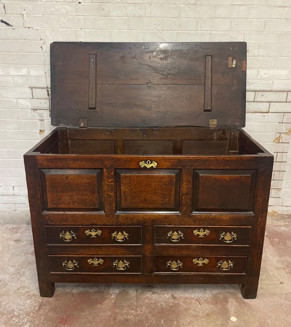 An 18th-century dark oak mule chest featuring three raised front panels above four brass-handled drawers, supported by stile feet. View V