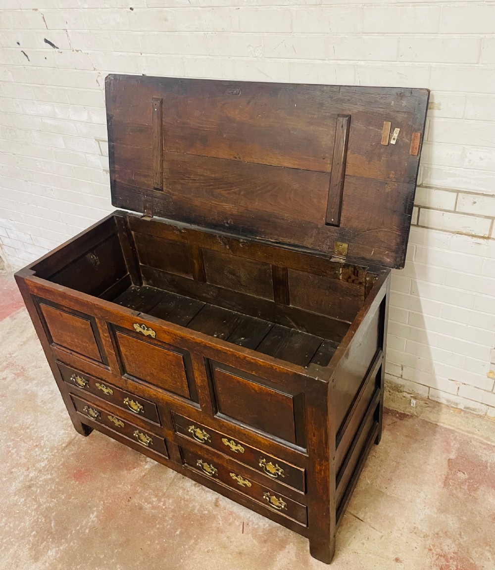 An 18th-century dark oak mule chest featuring three raised front panels above four brass-handled drawers, supported by stile feet. View VI