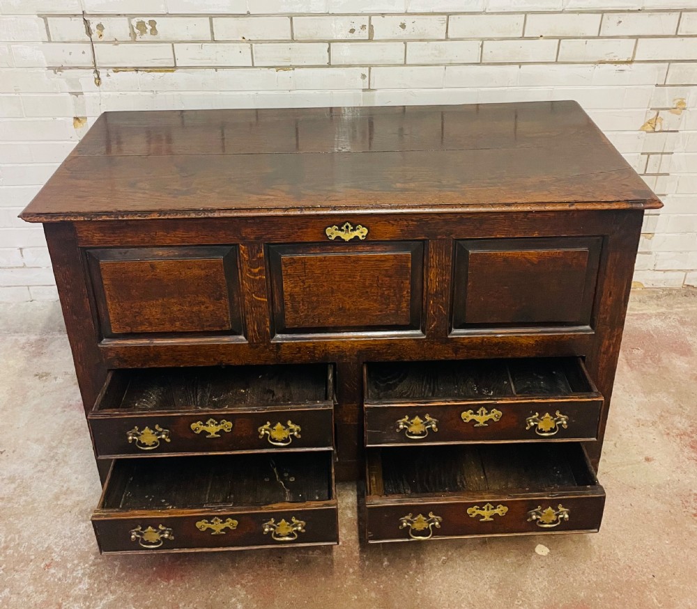 An 18th-century dark oak mule chest featuring three raised front panels above four brass-handled drawers, supported by stile feet. View X