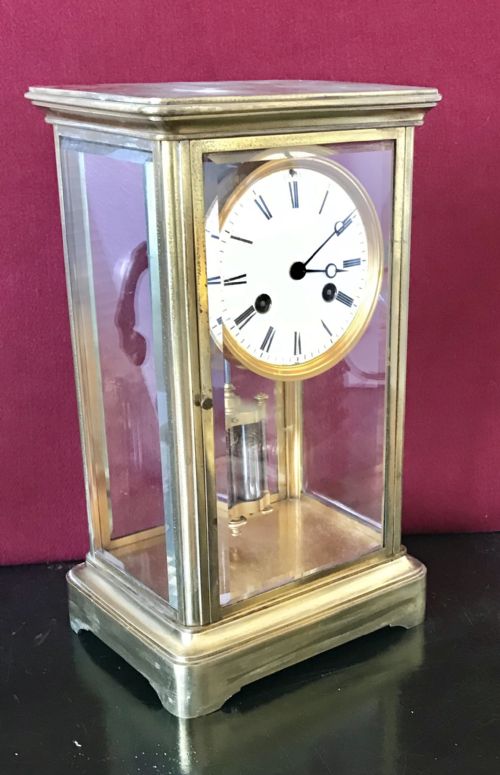 fig 1. A French four-glass mantel clock featuring a gilt brass case with bevelled glass panels, a white enamel dial with Roman numerals, and a visible pendulum.