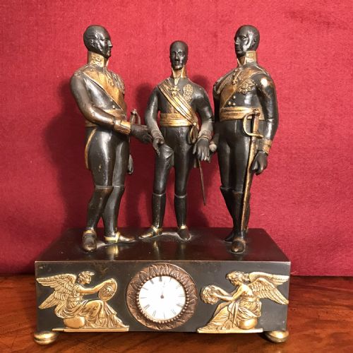 fig 1. A dark patinated bronze clock featuring three standing military figures on a rectangular plinth with gilt-bronze relief mounts and a circular dial.