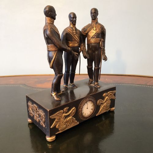 fig 2. A dark patinated bronze clock featuring three standing military figures on a rectangular plinth with gilt-bronze relief mounts and a circular dial.