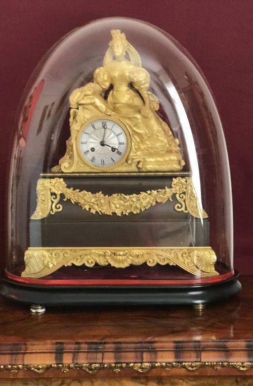 fig 1. A Regency period gilt bronze figural mantel clock depicting a woman seated beside a circular dial on an ebonised base with decorative swags.