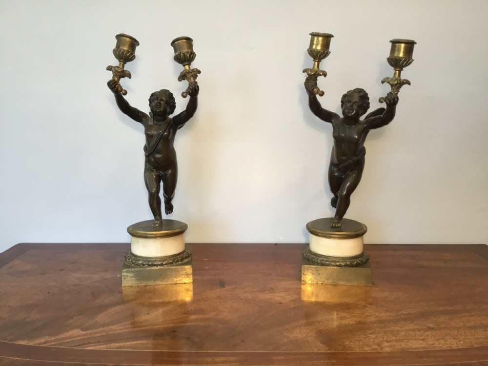 A pair of 19th-century French patinated bronze candelabra featuring putti holding two candle sconces each, mounted on round marble and square gilt metal bases.