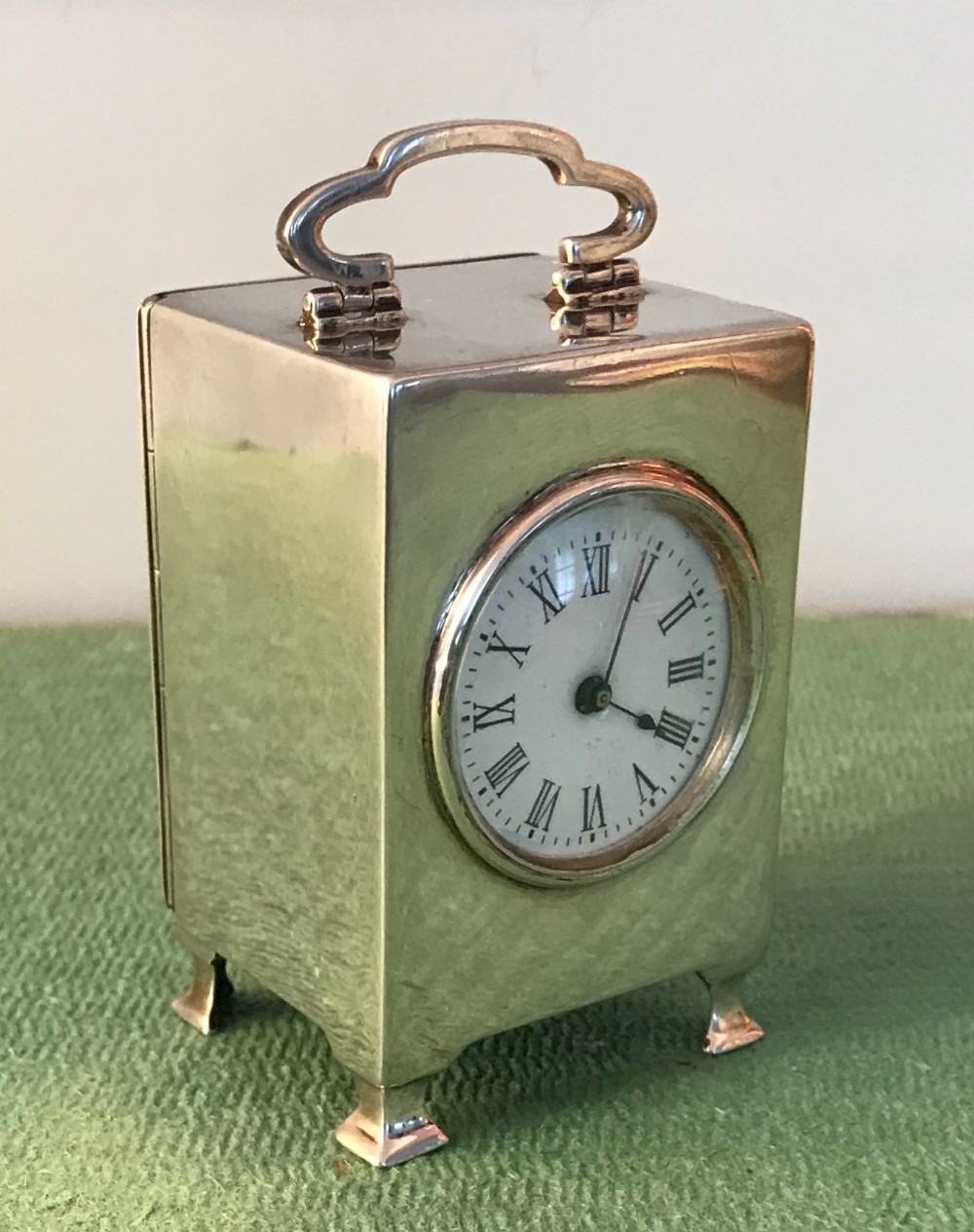 A small rectangular sterling silver miniature carriage clock with a hinged top handle, circular dial with Roman numerals, and bracket feet.