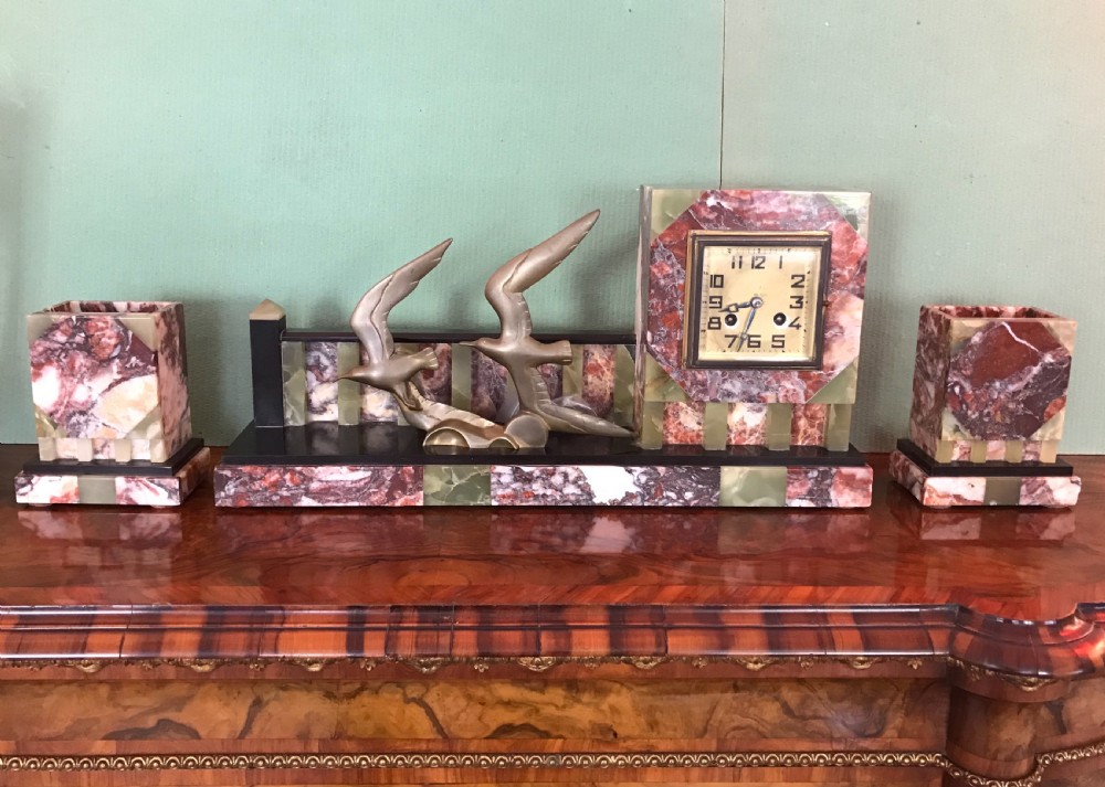 An Art Deco three-piece marble clock garniture set featuring a central clock with cast bronze birds in flight and two matching square side urns.