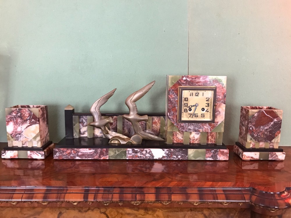 An Art Deco three-piece marble clock garniture set featuring a central clock with cast bronze birds in flight and two matching square side urns. View II