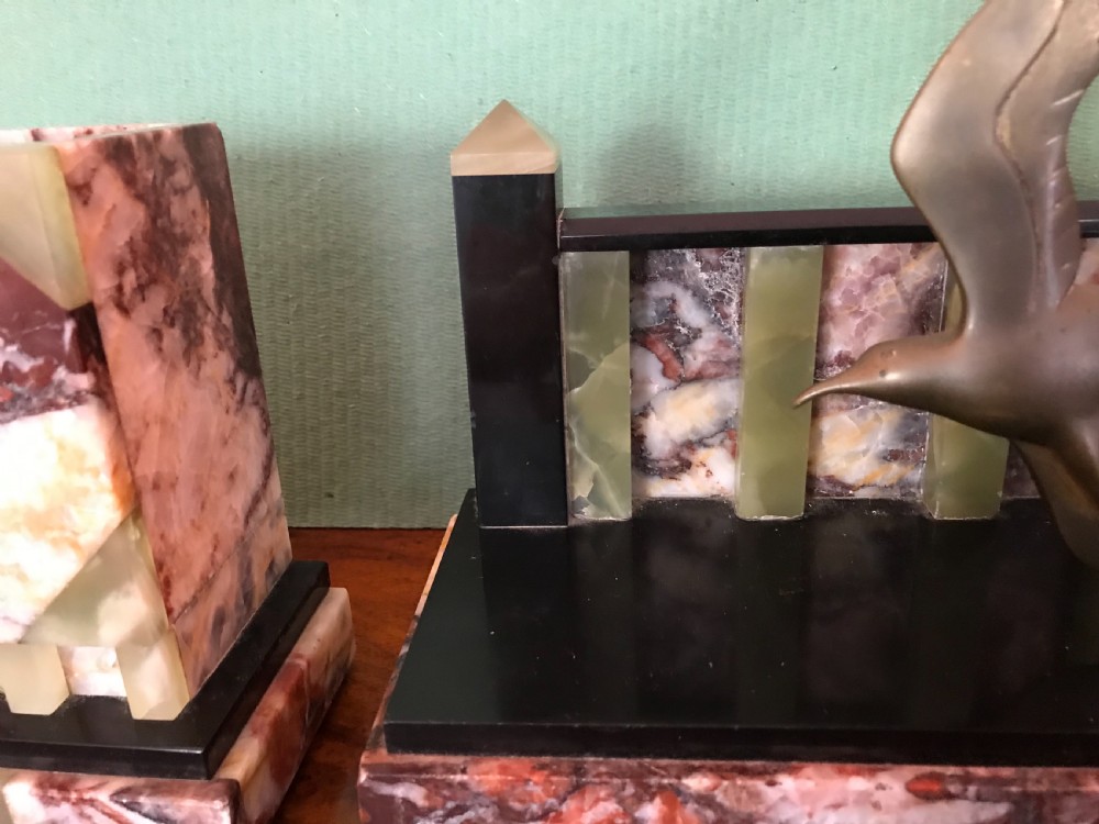 An Art Deco three-piece marble clock garniture set featuring a central clock with cast bronze birds in flight and two matching square side urns. View V