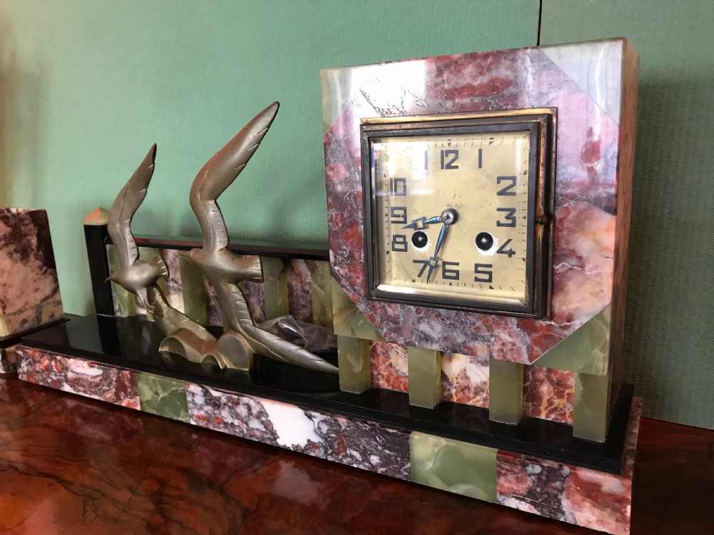 An Art Deco three-piece marble clock garniture set featuring a central clock with cast bronze birds in flight and two matching square side urns. View VI