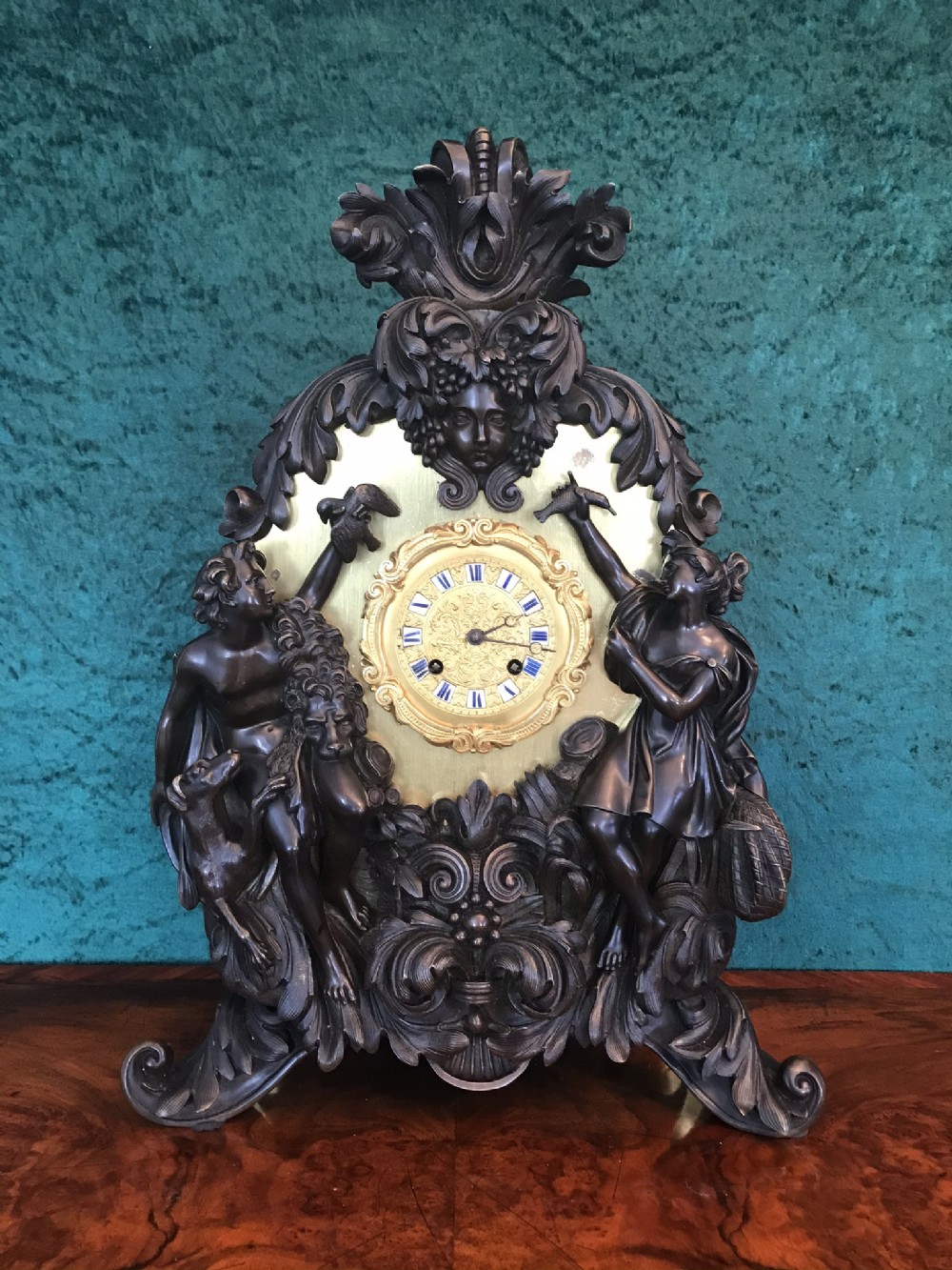 A Victorian patinated bronze mantel clock featuring classical figural sculptures, scrollwork ornamentation, and a gilt dial with enamel Roman numerals.