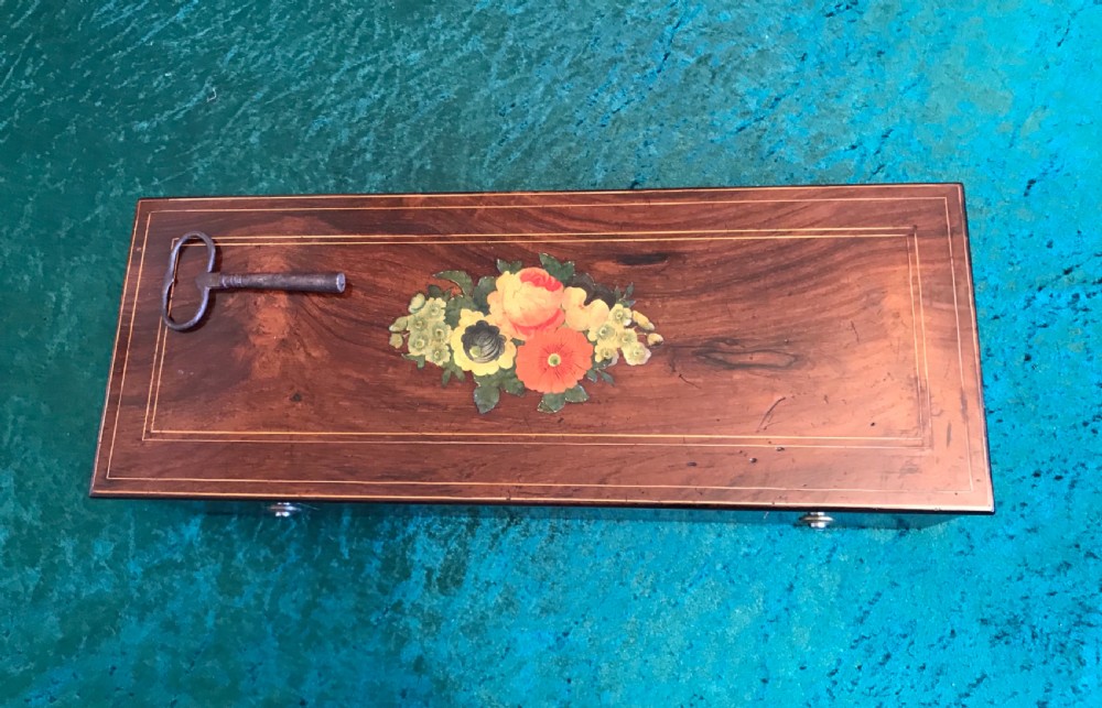 A rectangular dark wood music box with floral marquetry inlay on the lid and a metal winding key resting on top.
