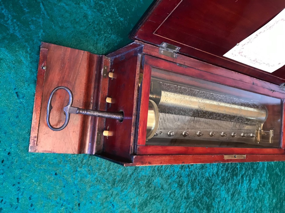 A rectangular dark wood music box with floral marquetry inlay on the lid and a metal winding key resting on top. View II