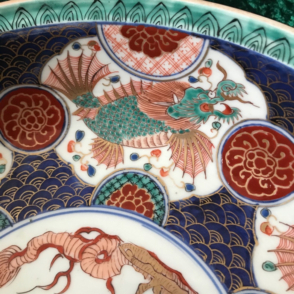 A circular antique Japanese Imari porcelain bowl decorated with a central dragon medallion surrounded by hand-painted fish, wave patterns, and floral motifs in blue, terracotta red, and turquoise. View III